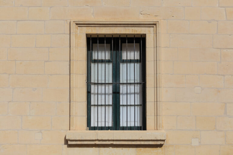 Malta, Valletta. Facade of yellow limestone house with closed window with metal bars, that provides safety. Close up view